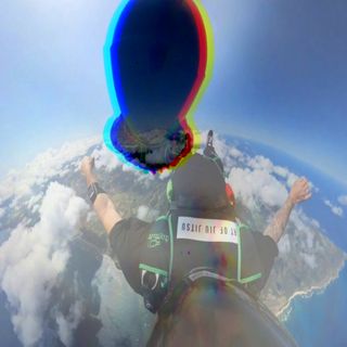 Two skydivers with black helmets face each other and descend towards earth thru a blue sky